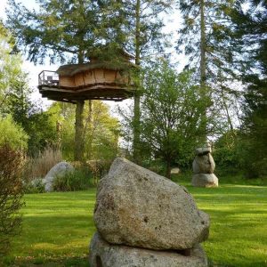 Cabane perchée dans les arbres en Bretagne, entourée de rochers et de verdure.