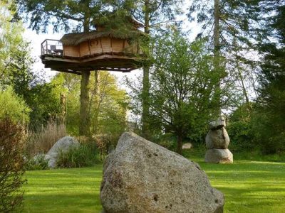 Cabane perchée dans les arbres en Bretagne, entourée de rochers et de verdure.
