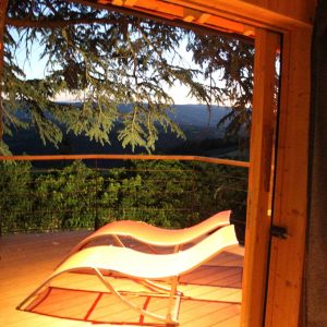 Cabane perchée en bois avec vue panoramique et transat sur la terrasse.