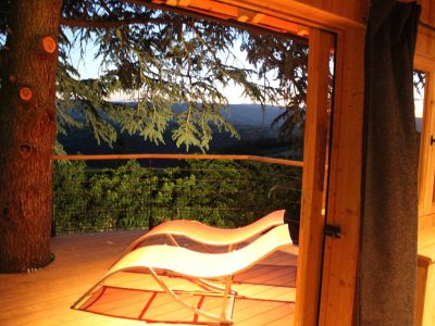 Cabane perchée en bois avec vue panoramique et transat sur la terrasse.