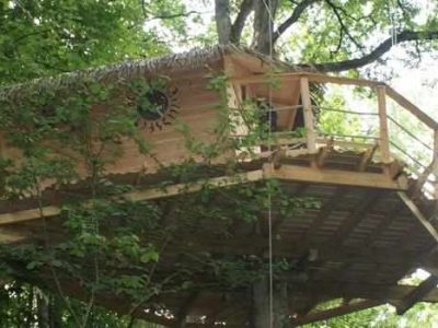 Cabane perchée dans les arbres, avec un balcon et un toit en chaume.