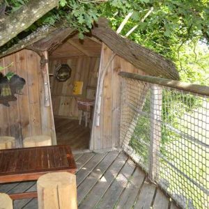 Cabane perchée dans les arbres, avec terrasse en bois et mobilier rustique.