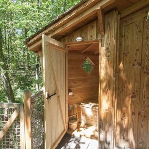 Cabane en bois perchée, avec une entrée en bois et vue sur la forêt verdoyante.