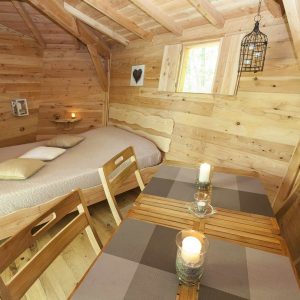 Cabane en bois cosy avec lit douillet et table en bois, ambiance chaleureuse.