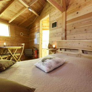 Cabane en bois chaleureuse avec lit douillet et lumière douce.