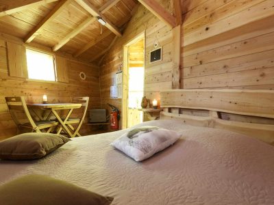 Cabane en bois chaleureuse avec lit douillet et lumière douce.