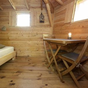 Cabane en bois chaleureuse avec lit douillet et table lumineuse.