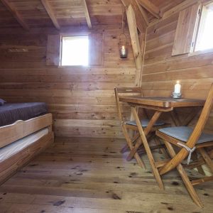 Hébergement insolite en bois avec lit confortable et table en bois, ambiance chaleureuse.