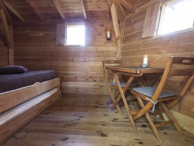 Hébergement insolite en bois avec lit confortable et table en bois, ambiance chaleureuse.
