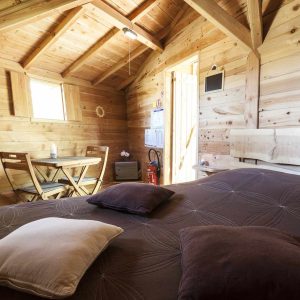 Cabane en bois cosy avec lit douillet et coin repas lumineux.