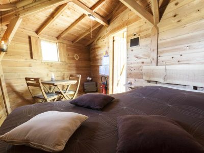 Cabane en bois cosy avec lit douillet et coin repas lumineux.