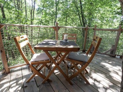 Cabane perchée en Auvergne-Rhône-Alpes avec terrasse en bois et vue sur la forêt.
