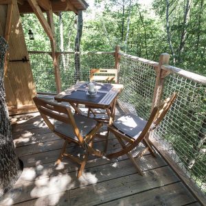 Cabane perchée en bois avec terrasse en bois et vue sur la forêt verdoyante.