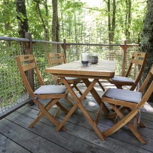 Cabane perchée en bois avec table et chaises sur une terrasse entourée darbres.