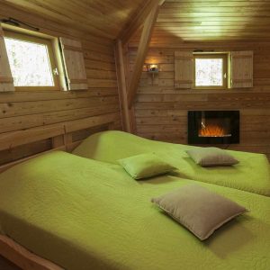 Chalet en bois avec lits douillets et cheminée, ambiance chaleureuse en Auvergne.