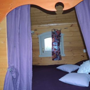 Cabane en bois à Limousin, avec un lit douillet et des rideaux violets.