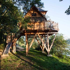 Cabane perchée en bois, entourée darbres, offrant une vue sur leau.