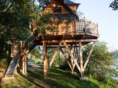 Cabane perchée en bois, entourée darbres, offrant une vue sur leau.