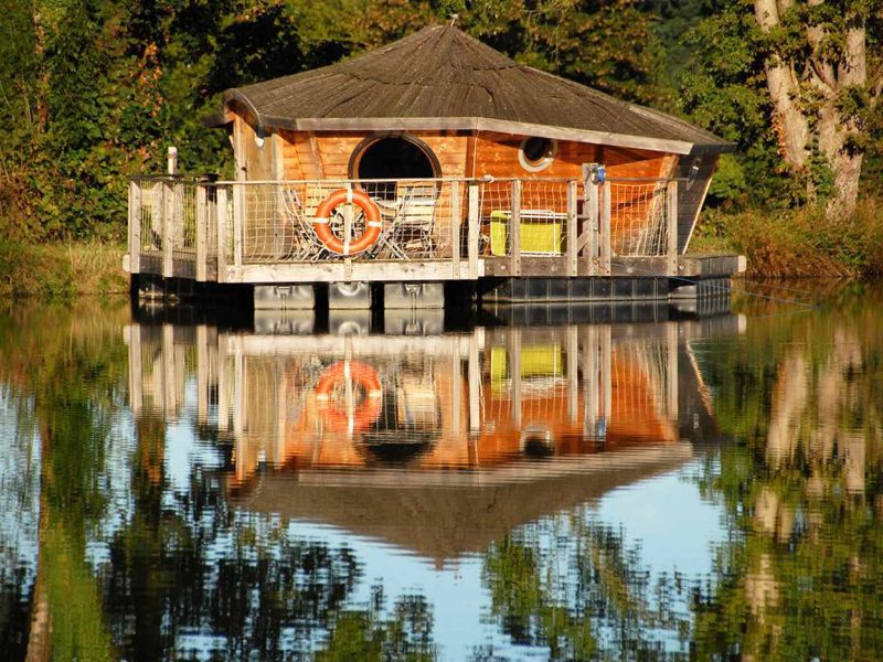 Cabane flottante en bois, entourée deau calme et de verdure luxuriante.