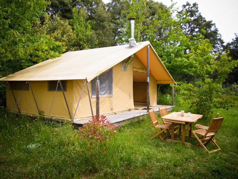 Tente safari spacieuse en pleine nature, avec terrasse et mobilier en bois.