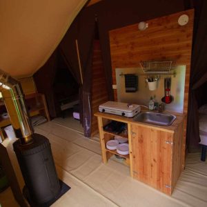 Tente lodge spacieuse avec coin cuisine et poêle à bois, idéale pour un séjour unique.