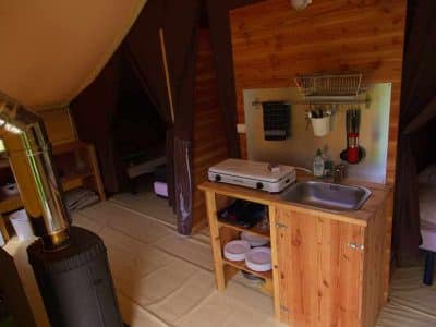 Tente lodge spacieuse avec coin cuisine et poêle à bois, idéale pour un séjour unique.