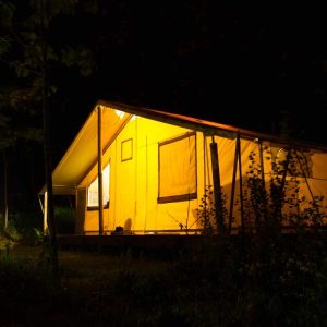 Tente safari lumineuse dans la nuit, entourée de verdure apaisante.