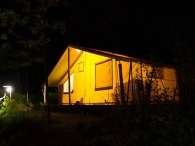 Tente safari lumineuse dans la nuit, entourée de verdure apaisante.