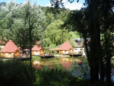 Hébergement insolite en cabanes en bois au bord dun étang, entouré darbres.
