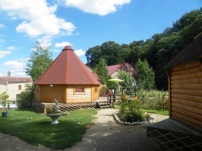 Cabane en bois ronde à Champagne-Ardennes, entourée de verdure et fleurs.