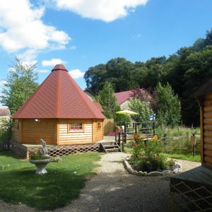 Cabane en bois rond à Champagne-Ardennes, entourée dun jardin verdoyant.