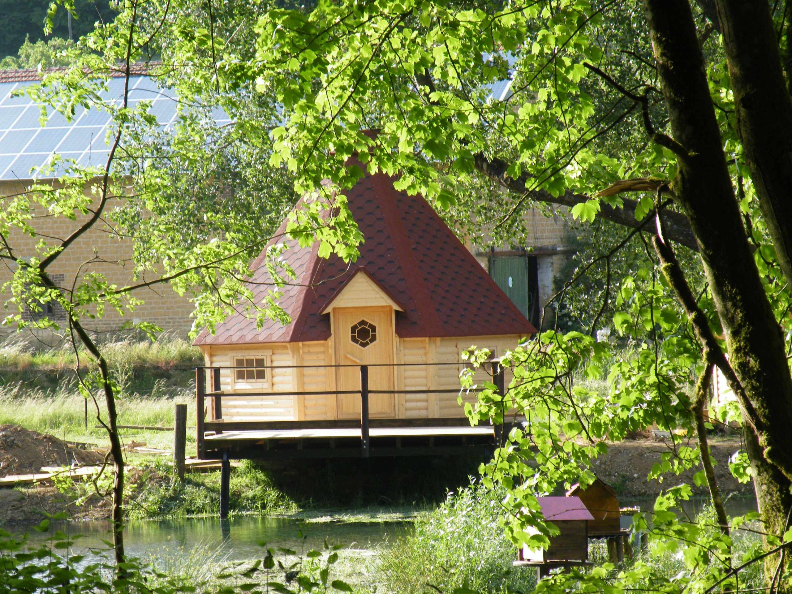 DSCF9494 Cabane en bois sur pilotis, entourée de verdure, au bord dun étang paisible.