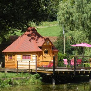 Cabane en bois au bord de leau, avec terrasse et parasols roses à Champagne-Ardennes.