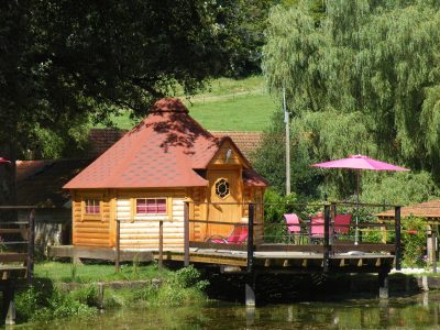 Cabane en bois au bord de leau, avec terrasse et parasols roses à Champagne-Ardennes.