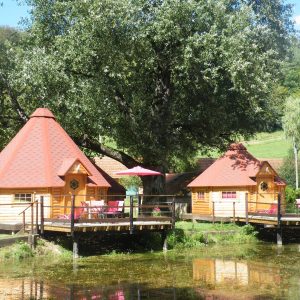 Cabane en bois sur pilotis, avec parasols roses, au bord dun étang paisible.