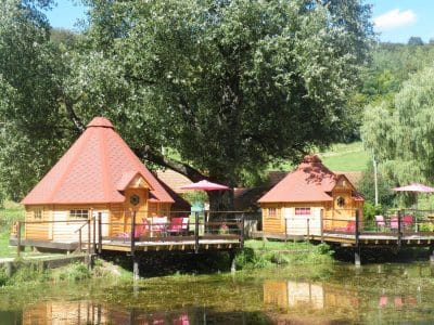 Cabane en bois sur pilotis, avec parasols roses, au bord dun étang paisible.