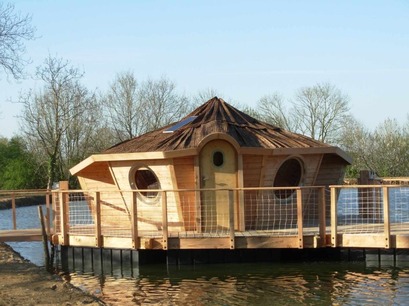 Cabane flottante en bois avec un toit en pente et de grandes fenêtres rondes.