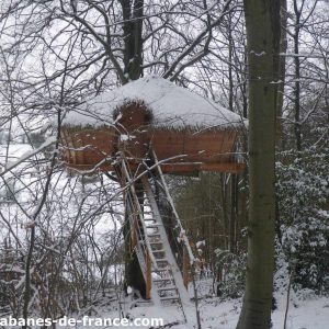 Cabane perchée en bois, entourée de neige et darbres en Haute-Normandie.