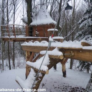 Cabane perchée en bois, entourée de neige et de sapins en Haute-Normandie.