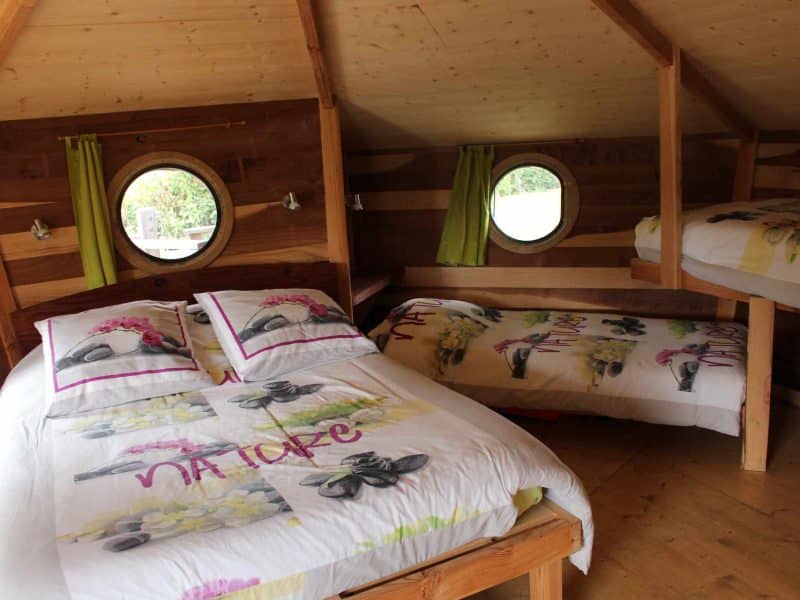 Chalet en bois chaleureux avec lits douillets et fenêtres rondes.