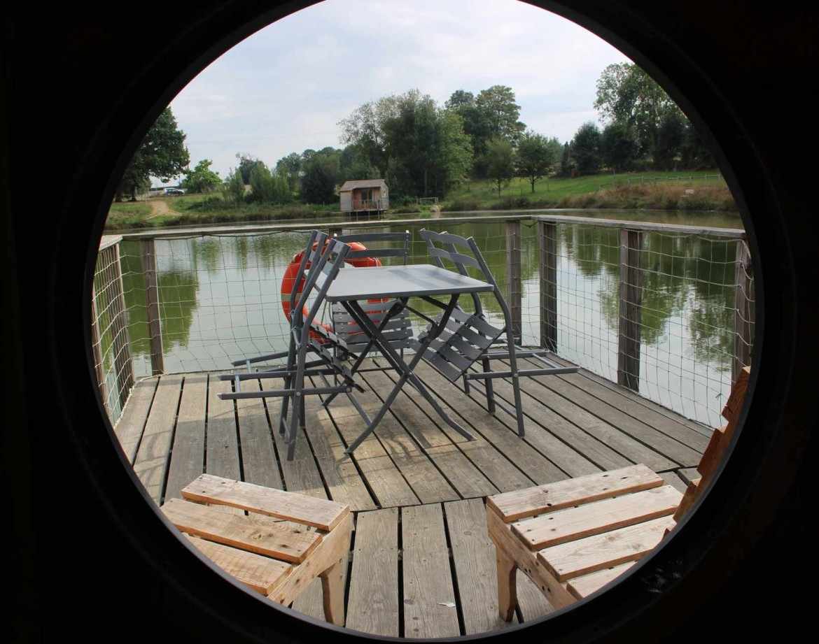 Hébergement insolite : un bateau sur leau avec une terrasse en bois et des chaises.