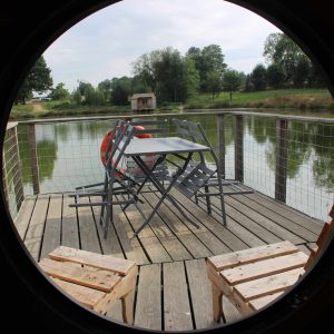 Hébergement insolite : un bateau sur leau avec une terrasse en bois et des chaises.