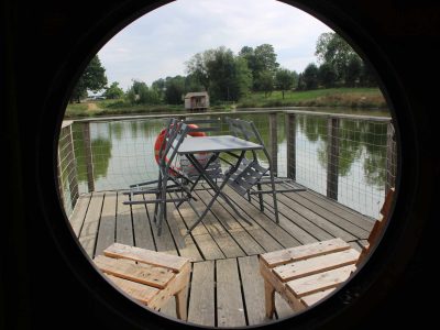 Hébergement insolite : un bateau sur leau avec une terrasse en bois et des chaises.