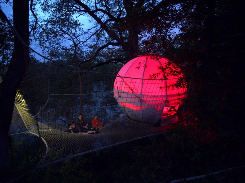 Hébergement insolite en bulle suspendue, illuminée par des lumières rouges dans les arbres.