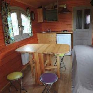 Cabane en bois à Limousin, intérieur chaleureux avec table en bois et coussins colorés.