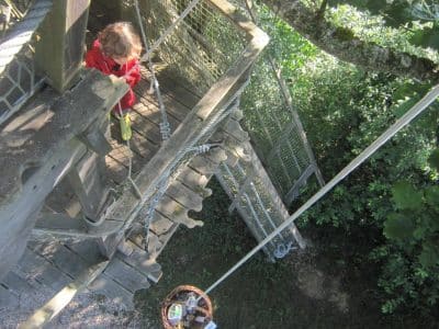 Cabane perchée dans les arbres, avec un enfant jouant sur une plateforme en bois.