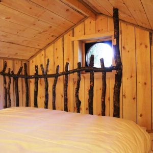 Cabane en bois avec un lit douillet et des éléments en branches naturelles.