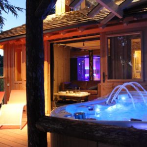 Chalet en bois avec jacuzzi illuminé, entouré de nature paisible.