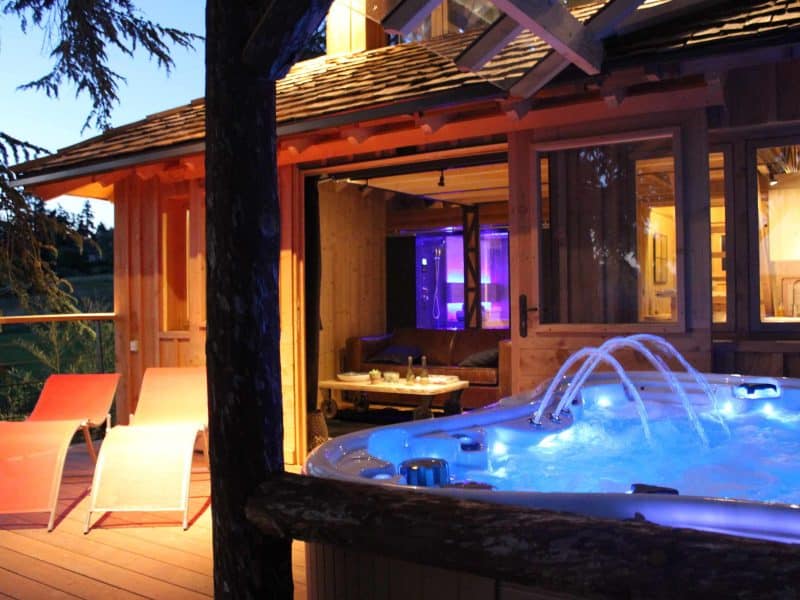 Chalet en bois avec jacuzzi illuminé, entouré de nature paisible.