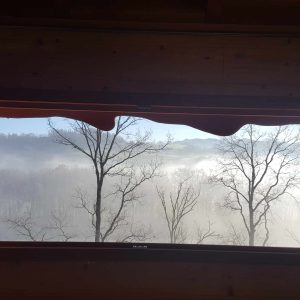 Vue depuis un chalet en bois, entouré de brume et de paysages verdoyants.